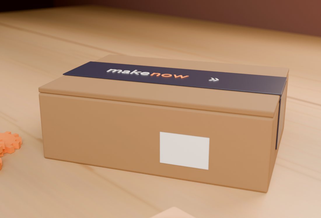 MakeNow shipping box with branded tape, with 3D printed parts on a workshop table